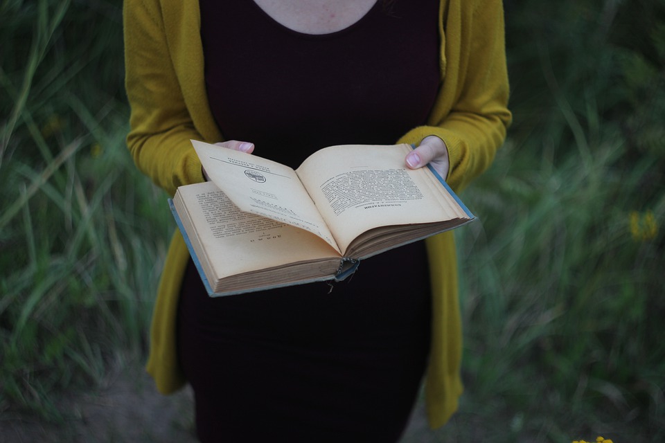woman in black dress and yellow sweater holding open book